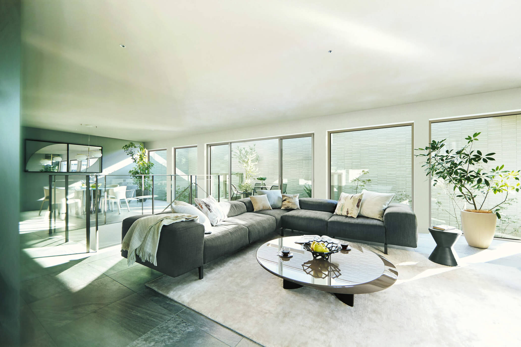 大開口の窓とグレーのソファが印象的な広々としたリビング。自然光が降り注ぐ明るい空間