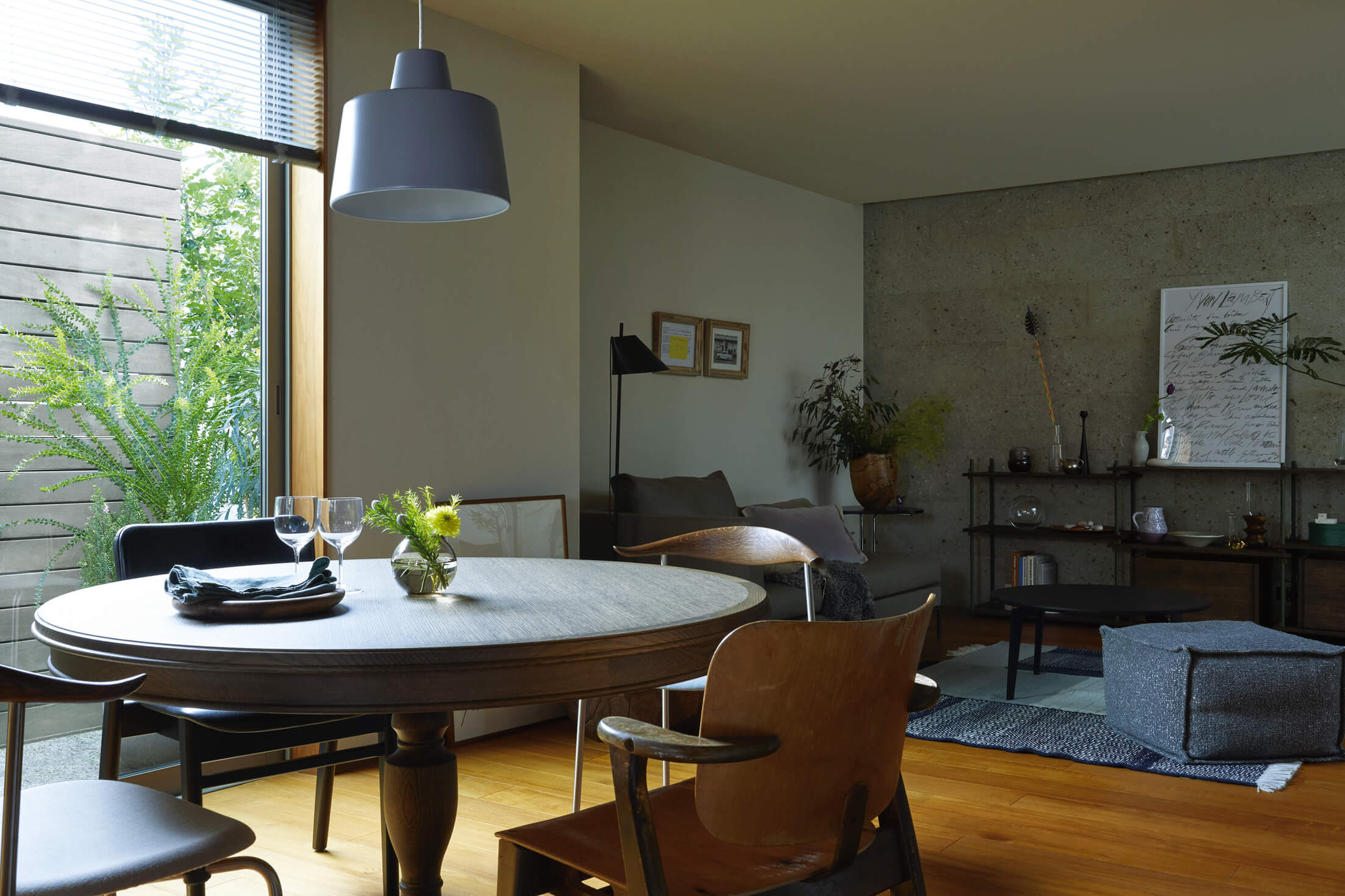 丸テーブルのあるダイニングとグレーソファのリビング。コンクリート壁が印象的なモダン空間