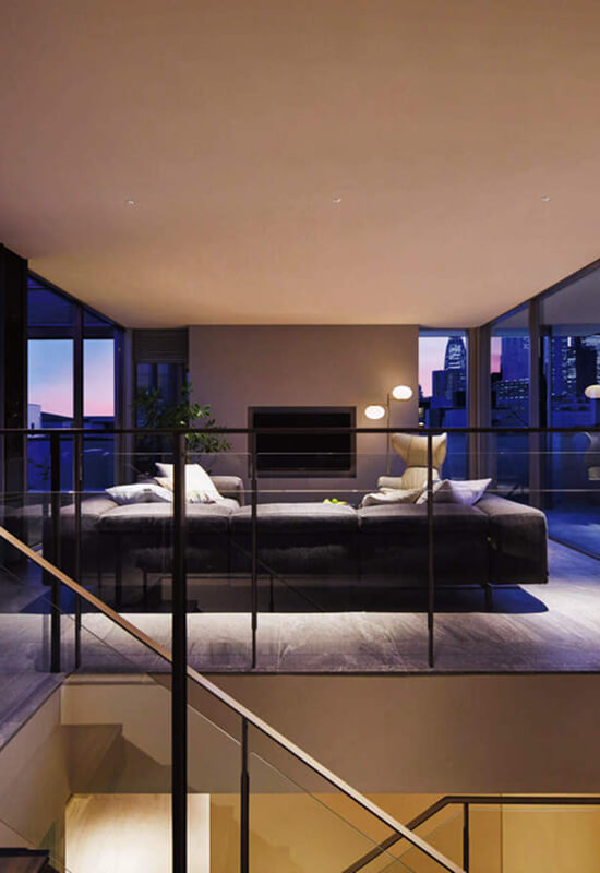 夕暮れ時のガラス張りリビング。都市の夜景を望む洗練されたモダン空間