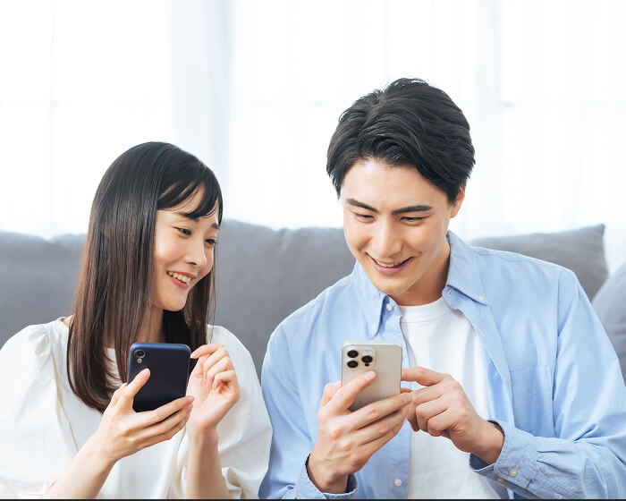 スマートフォンで相談予約をする若いカップル。WEBから簡単に予約できる様子